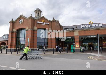 Mann in gelber reflektierender Weste, der mit Einkaufskörben auf dem Parkplatz des Morrisons Supermarkts Starbeck Store läuft Stockfoto