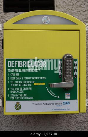 Nahaufnahme eines gelben Defibrillatorkastens an einer Wand in Knaresborough Yorkshire, Großbritannien Stockfoto