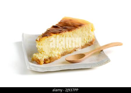 Käsekuchen, klassischer New Yorker Käsekuchen auf Holzhintergrund. Scheibe leckeren Kuchen auf weißem Teller und Holzlöffel isoliert auf weiß, backen Stockfoto