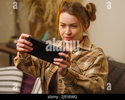 Ein junges Mädchen spielt Videospiele auf einer tragbaren Spielkonsole. Nahaufnahme, beige Töne. Zimmereinrichtung. Virtual Reality, Cyberspace, eSports, Jugendkultur, Stockfoto