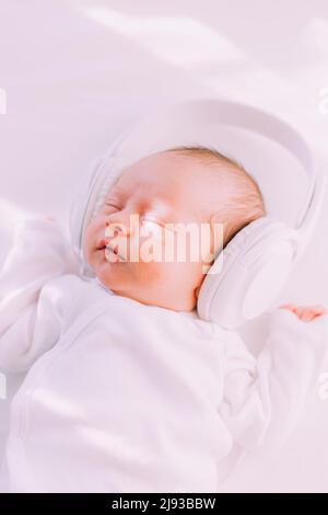 Das Kind trägt Kopfhörer. Frohes Baby. Ein neugeborenes Baby. Weiß auf Weiß Stockfoto