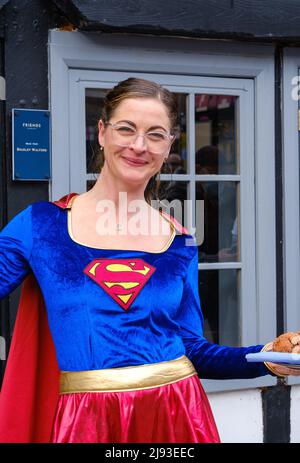 Ein Mitarbeiter des Friends Restaurant in Superwoman-Kostümen lächelt und hält ein Tablett mit Speisen bei der 2022 St. George's Day-Fest, Pinner, London Stockfoto