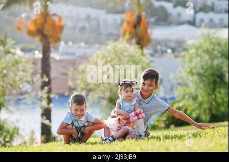 Drei Kinder sitzen auf Gras im Turkey Resort gegen Palmen. Stockfoto