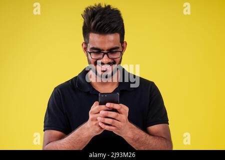 Lächelnder, hübscher inder, der Selfie auf gelbem Hintergrund fotografiert Stockfoto