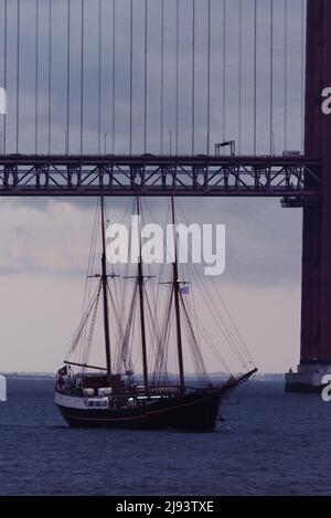 Segelschiff, das an der Brücke vom 25. April über den Fluss Tejo in Lissabon, Portugal, vorbeifährt Stockfoto