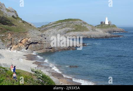 Der Strand an der Bracelet Bay mit Leuchtturm und Murmeln bei Flut an einem sonnigen Tag gehen Besucher den Küstenpfad entlang Stockfoto