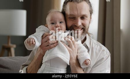 Liebevoller Erwachsener bärtiger Vater hält Baby neugeboren fürsorglich Vater spielt mit kleinen Tochter Sohn Kind springen lachenden Mann küssen Kind im Kopf zusammen p Stockfoto