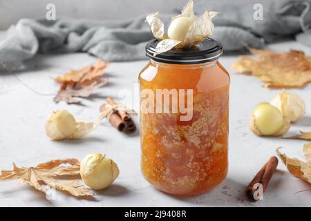 Hausgemachte, transparente Physalis-Marmelade mit Zimt im Glas auf grauem Hintergrund Stockfoto