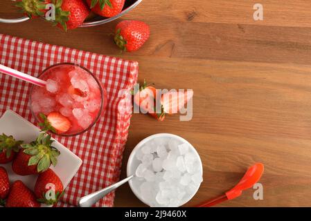 Obstgranita mit reifen Erdbeeren mit viel Eis auf Holztisch mit Schüssel mit Eis und Korb voller Erdbeeren. Draufsicht. Horizontaler Kompost Stockfoto