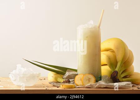 Bananengranita mit Früchten um auf Holztisch mit Schale aus Eis und weißem isolierten Hintergrund. Vorderansicht. Horizontale Zusammensetzung. Stockfoto