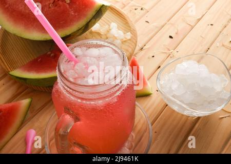 Glas mit natürlicher Wassermelone Getränk mit Eis auf einem Holztisch mit Früchten um. Erhöhte Ansicht. Horizontale Zusammensetzung. Stockfoto