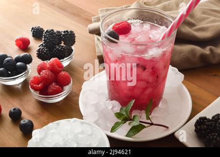 Fruchtgetränk mit Brombeeren, Himbeeren und Heidelbeeren auf Holztisch mit Behältern voller Früchte und Eis. Erhöhte Ansicht. Horizontale Kompositio Stockfoto