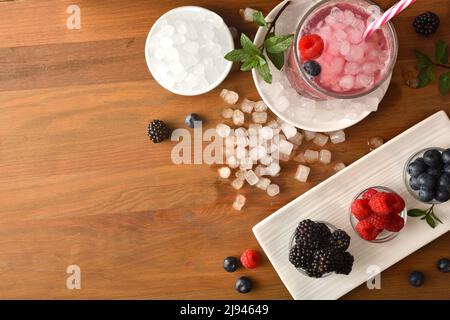Hintergrund mit kaltem Getränk von Waldfrüchten mit Obst und Eis herum. Draufsicht. Horizontale Zusammensetzung. Stockfoto