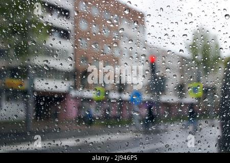 Regentropfen auf der Windschutzscheibe im Hintergrund der Stadtstraße Stockfoto