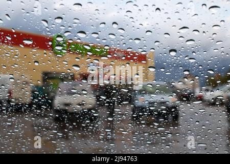 Regentropfen auf der Windschutzscheibe im Hintergrund der Stadtstraße Stockfoto