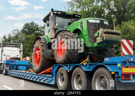 POV schweren Flurförderzeug Sattelauflieger Flachbett Plattform Transport einer großen modernen Landwirtschaft Traktor Maschine auf gemeinsame Autobahn Straße bei hellem Himmel Stockfoto