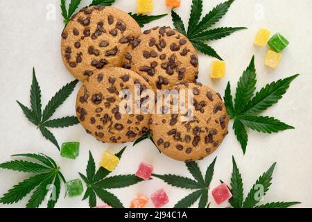 Amerikanische Cookies mit Cannabisextrakt. Süßigkeiten mit CBD-Öl. Marihuana Blätter auf weißem Hintergrund. Draufsicht, flach liegend. Stockfoto