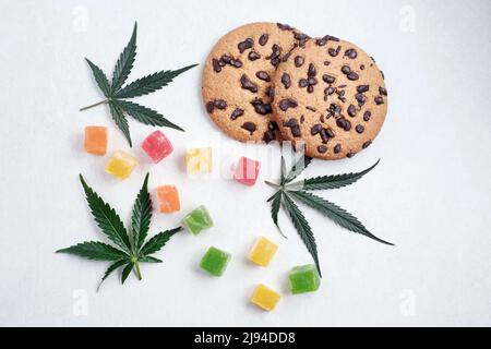 Amerikanische Cookies mit Cannabisextrakt. Süßigkeiten mit CBD-Öl. Marihuana Blätter auf weißem Hintergrund. Draufsicht, flach liegend. Stockfoto