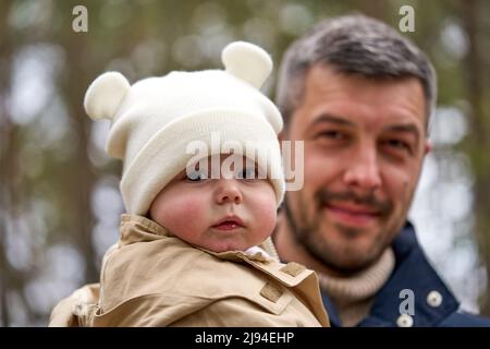 Vater hält Tochter an den Händen. Sie schauen auf die Kamera und lächeln. Das Gesicht des Vaters ist unfokused. Stockfoto