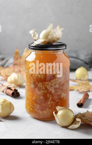 Hausgemachte transparente Physalis-Marmelade mit Zimt in einem Glas auf hellgrauem Hintergrund, vertikales Format Stockfoto