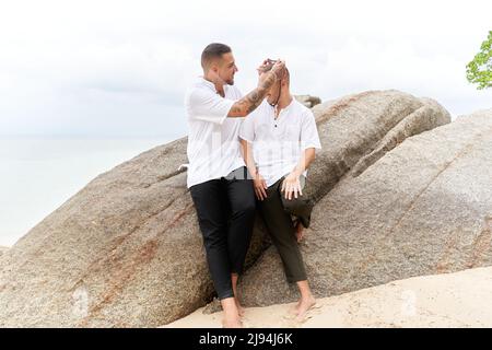 Mann, der an einem tropischen Strand eine Halskette um den Hals seines schwulen Partners legt Stockfoto