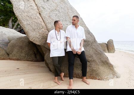 Schwule Paare stehen an einem Strand in weißen und schwarzen Freizeitkleidung Stockfoto