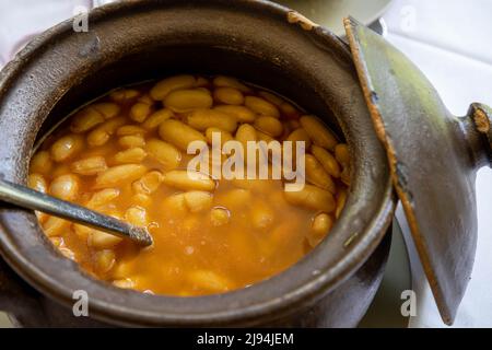 Große weiße Bohnen aus einem asturischen Bohneneintopf in einem Tontopf. Typisch spanisches Essen. Stockfoto