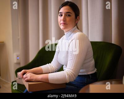 Erwachsene Frau sitzt auf einem Sofa mit der Box ihres neuen Produkts in einem Coworking Space, Portrait Stockfoto