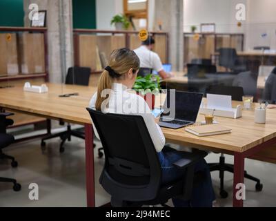 Frau mit ihrem Mobiltelefon sitzt in einem Coworking Space mit anderen Menschen Stockfoto