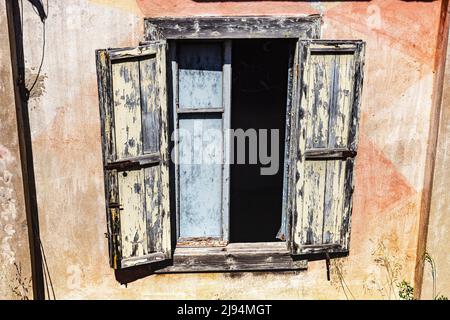 Außenfenster und gebleichte hölzerne Fensterläden Detail in Batteria Battistoni, einem verunglückten Gebäude aus dem Jahr WW2, am Rand der Klippe; Baia Sardinia, Sardinia, Italien. Stockfoto