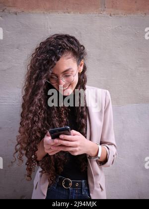 Porträt einer lächelnden jungen Frau, die ihr Mobiltelefon hält und mit ihr chattet, vertikale Fotografie von der Hüfte nach oben Stockfoto