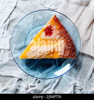 Blick aus der Perspektive auf ein Stück Coca de sant joan, eine typische süße flache Torte aus katalonien, spanien, gegessen am saint johns Eve, serviert in einem blauen Glas pla Stockfoto