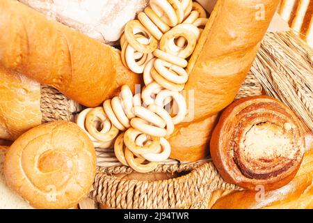 Kulinarischer Hintergrund mit Brot, Brötchen, trocknenden Bagels, Weizenohren in einem Korbkorb, Draufsicht Stockfoto
