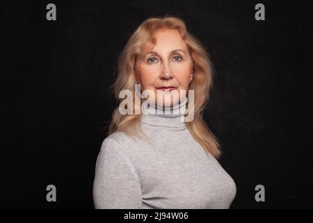 Blonde Frau mit grauem Rollkragen auf schwarzem Wandhintergrund Stockfoto