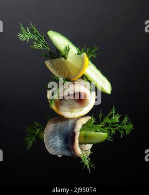 Heringsfilet in Öl mit Zitrone, Gurke und Dill auf dunklem Grund. Stockfoto
