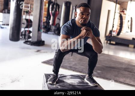 afroamerikanischer junger Boxer schaut weg, während er sich im Fitnessstudio in die Hocke hockt Stockfoto