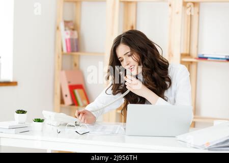 Ernst gut gekleidete Verkäuferin am Telefon sprechen im Büro hinter ihrem Schreibtisch und Laptop. Platz kopieren Stockfoto