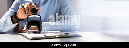 Nahaufnahme von einer Person Hand Stanzen mit Genehmigt Stempel auf Dokument am Schreibtisch Stockfoto