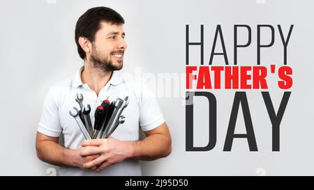 Lächelnder, glücklicher bärtiger Mann mit einem Strauß Schraubenschlüssel, Schraubenschlüsseln und Schraubendrehern mit Inschrift Happy Father's Day. Happy Fathers Day Konzept oder Greeti Stockfoto