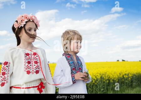 Junge und ein Mädchen in bestickter traditioneller Kleidung vor dem Hintergrund des gelb blühenden Rapsfeldes. Einheit, Unterstützung für die Ukraine. Die Ukrainer sind wieder da Stockfoto