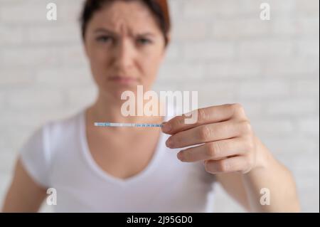 Unglückliche Frau zeigt einen schnellen negativen Test auf Eisprung. Das Konzept der Verletzung der weiblichen Fortpflanzungsfunktion. Frustriertes Mädchen. Luteinisierend Stockfoto