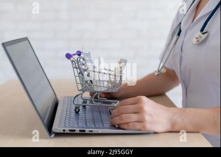 Unkenntlich Frau Arzt auf Online-Konsultation für Laptop. Online-Apotheke Konzept. Der gesichtslose Apotheker legt die Medizin in einen Mini-Warenkorb. Stockfoto