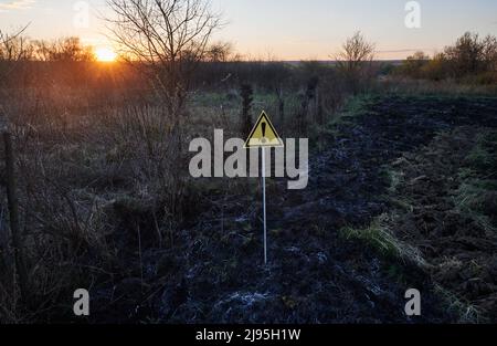 Verbranntes trockenes Gras und Warnschild mit Ausrufezeichen warnen vor gefährlichen Feldbedingungen bei Sonnenuntergang. Konzept von Ökologie und Naturkatastrophen. Stockfoto