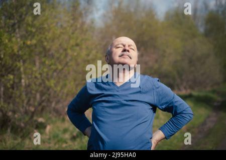 Senior Läuferin mit Armband beim Stretching, beim Atmen frischer Luft. Frühling Natur. Gesunde Lebensweise im Alter. Stockfoto