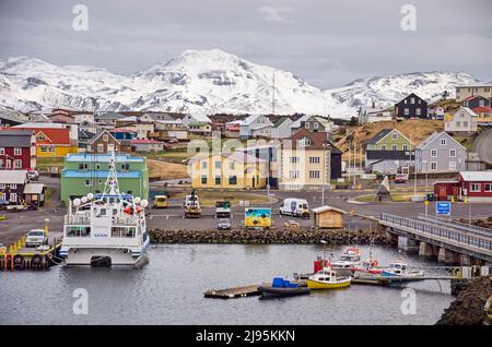 Stykkishólmur, Island, 4. Mai 2022: Lebendige Szene mit dem Hafen, den bunten Häusern der Stadt und den schneebedeckten Bergen dahinter Stockfoto