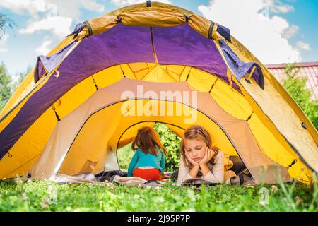 Kleine Kinder, Kinder spielen, lesen Buch im orangen Touristenzelt. Familienausflug, Wanderung in die Natur. Hinterhof-Spiele, Spaß haben. Erholung im Freien, Aktivität. Sel Stockfoto