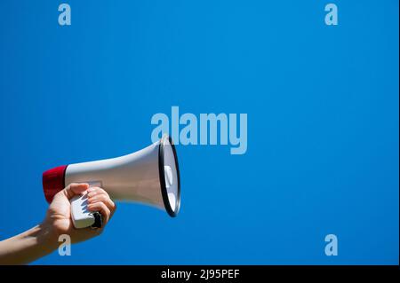 Megaphon in einer weiblichen Hand auf blauem Hintergrund. Keine Personen. Zugeschnittenes Foto. Eine Frau hält einen Schallverstärker gegen den Himmel. Stockfoto