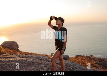 Eine Trailrunnerin hält eine Mütze, während sie auf einem Hügel hinaufgeht Stockfoto