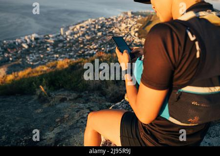 Nahaufnahme Frau Wandererin in Sportlothes überprüft Smartphone, während sie auf dem Gipfel des Berges bei Sonnenuntergang sitzt Stockfoto