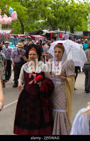 Madrid, Spanien; 15.. Mai 2022: Eine Gruppe von Leuten besucht die Stände auf der Messe Saint Isidro. 2 Frauen mit dem Rücken bekleidet im traditionellen M Stockfoto